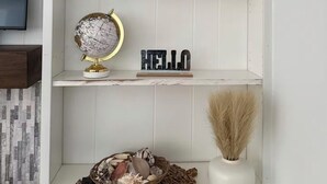 Et hvidt reolsystem med dekorative genstande, herunder en globus, et skilt med 'HELLO', et skilt med 'RELAX' og et lille fuglehus.