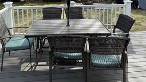 En træterrasse med et bord, stole og en parasol, samt et træhegn i baggrunden.
