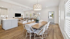 A spacious kitchen with a central island, a dining area with wicker chairs, and a large pendant light. - 🎥 Outdoor Movie Screen | Fire Pit | Games | Bikes | Sleeps 10 - Bike to Beach! (Inlet Beach)