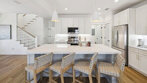 A modern kitchen with a central island, stainless steel appliances, and a staircase leading to another level. - 🎥 Outdoor Movie Screen | Fire Pit | Games | Bikes | Sleeps 10 - Bike to Beach! (Inlet Beach)