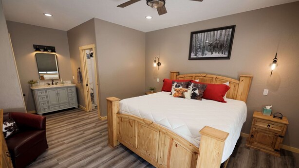 A bedroom with a wooden bed, a red chair, a vanity with a mirror, and a framed picture on the wall.