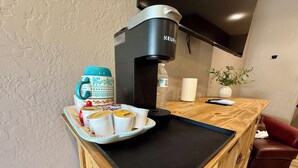 A kitchenette with a coffee maker, a water bottle, a mug, a tray with cups, and a plant.