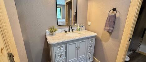 Une salle de bain avec un lavabo en marbre, un miroir avec éclairage intégré, une plante en pot et un porte-serviettes.