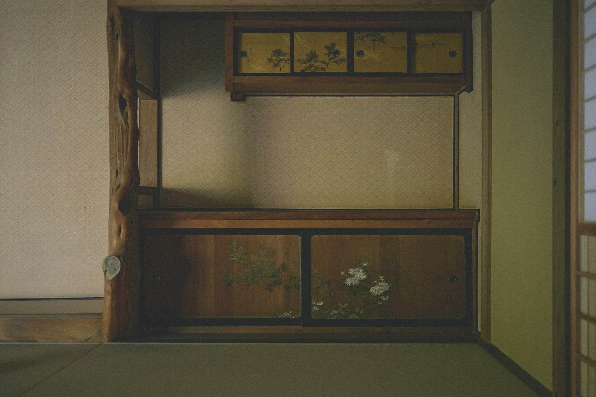 Une pièce de style japonais traditionnel, avec un sol recouvert de tatamis, un meuble en bois orné de motifs floraux et une porte coulissante.