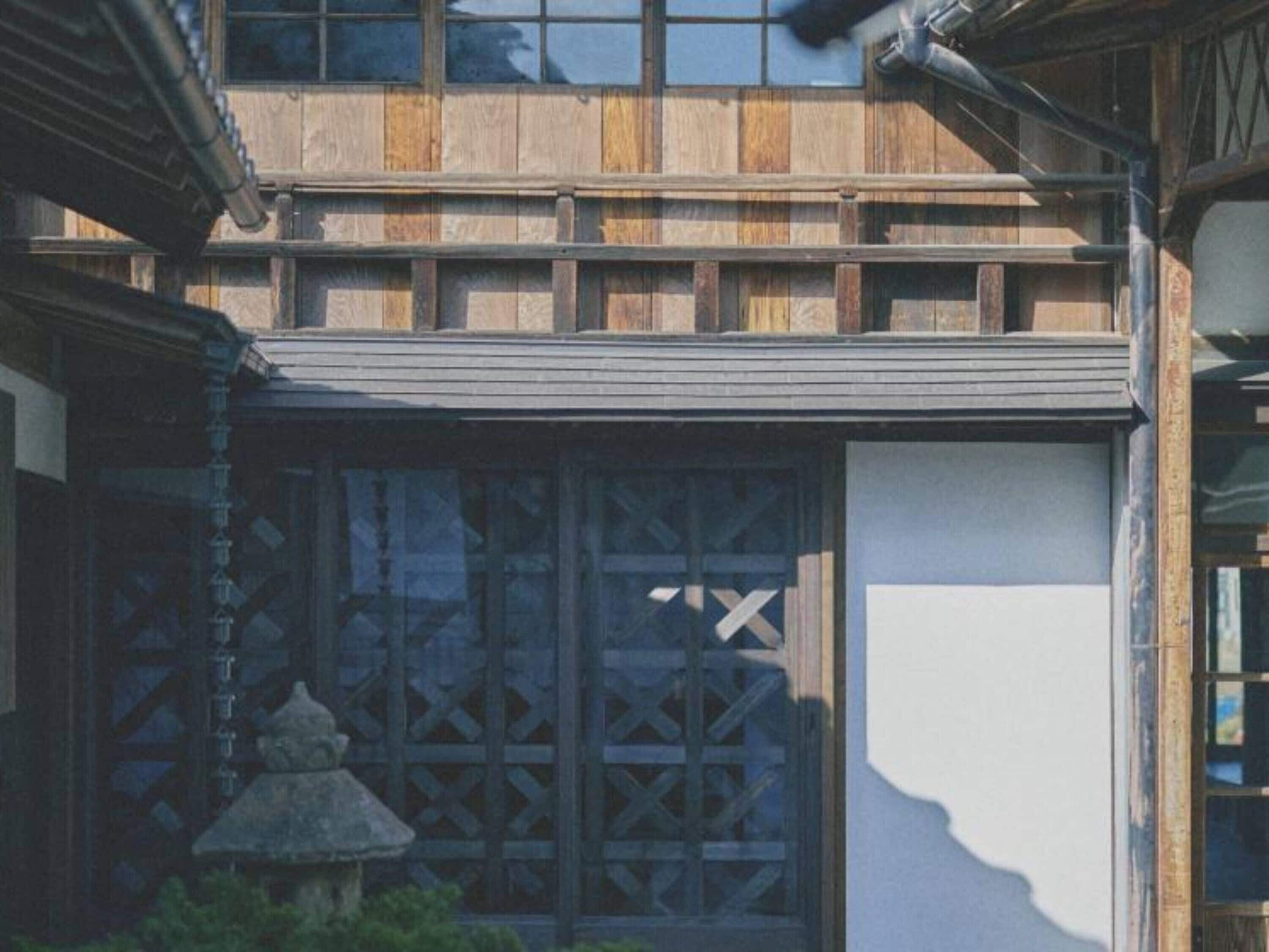 A traditional building with a wooden facade, large windows with lattice designs, and a stone lantern.