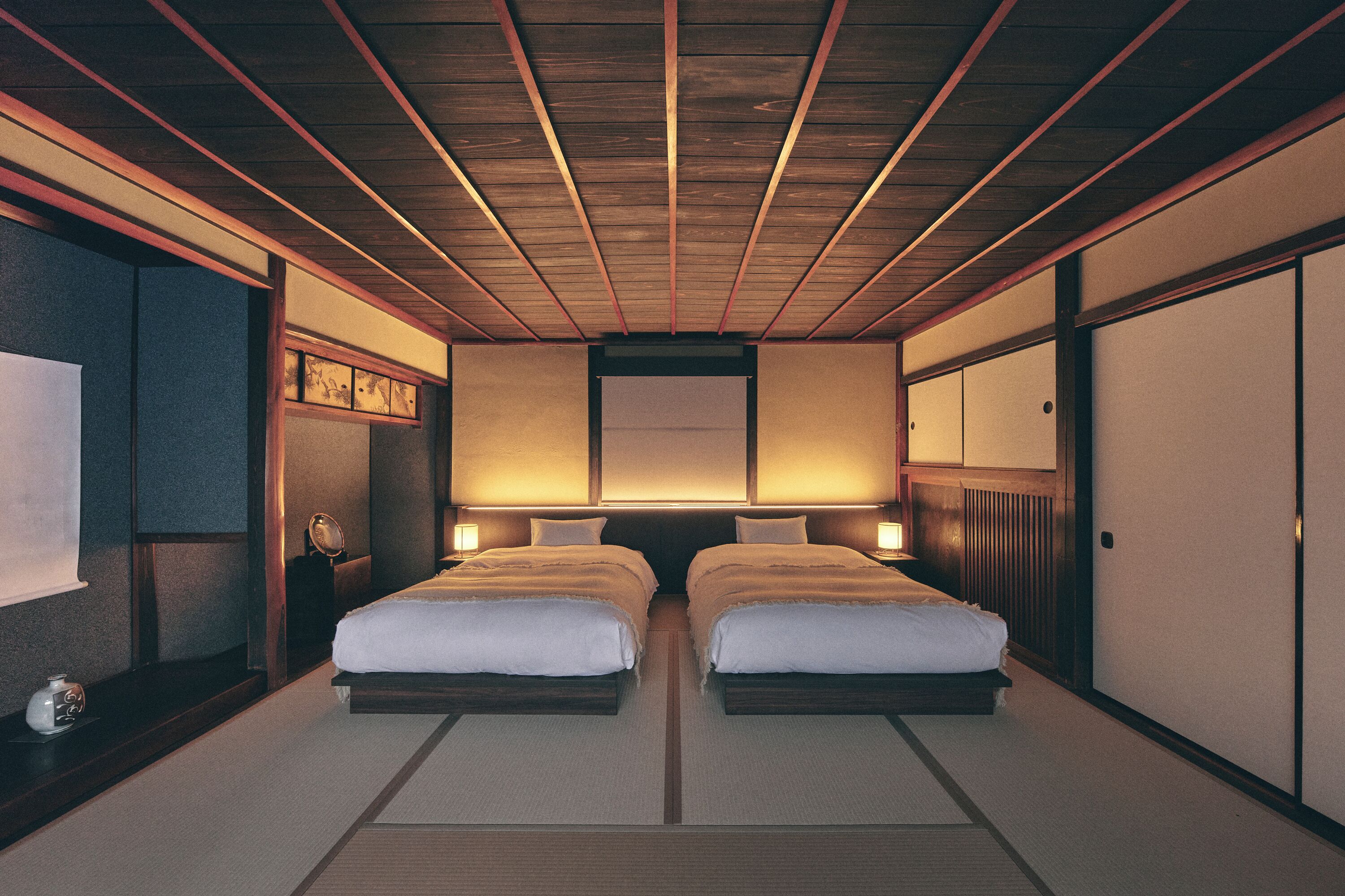 Una habitación tradicional japonesa con suelo de tatami, dos camas, vigas de madera en el techo y puertas correderas.