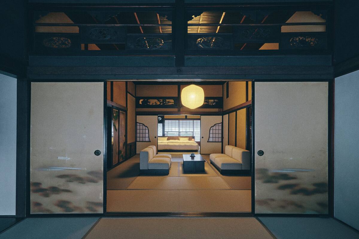A traditional Japanese-style room with tatami flooring, a low table, and a bed with a futon.