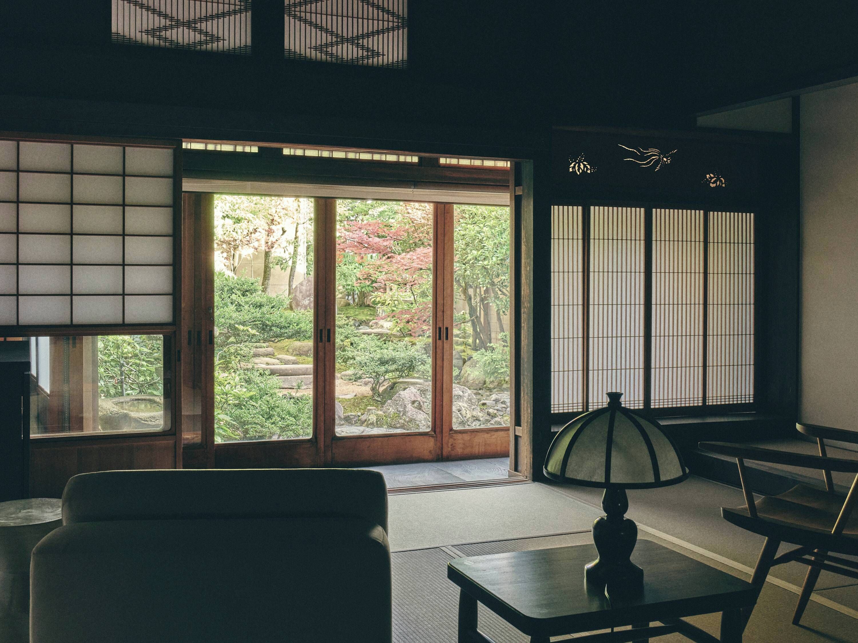 A traditional Japanese room with tatami flooring, a low table with a lamp, and sliding doors leading to a garden.