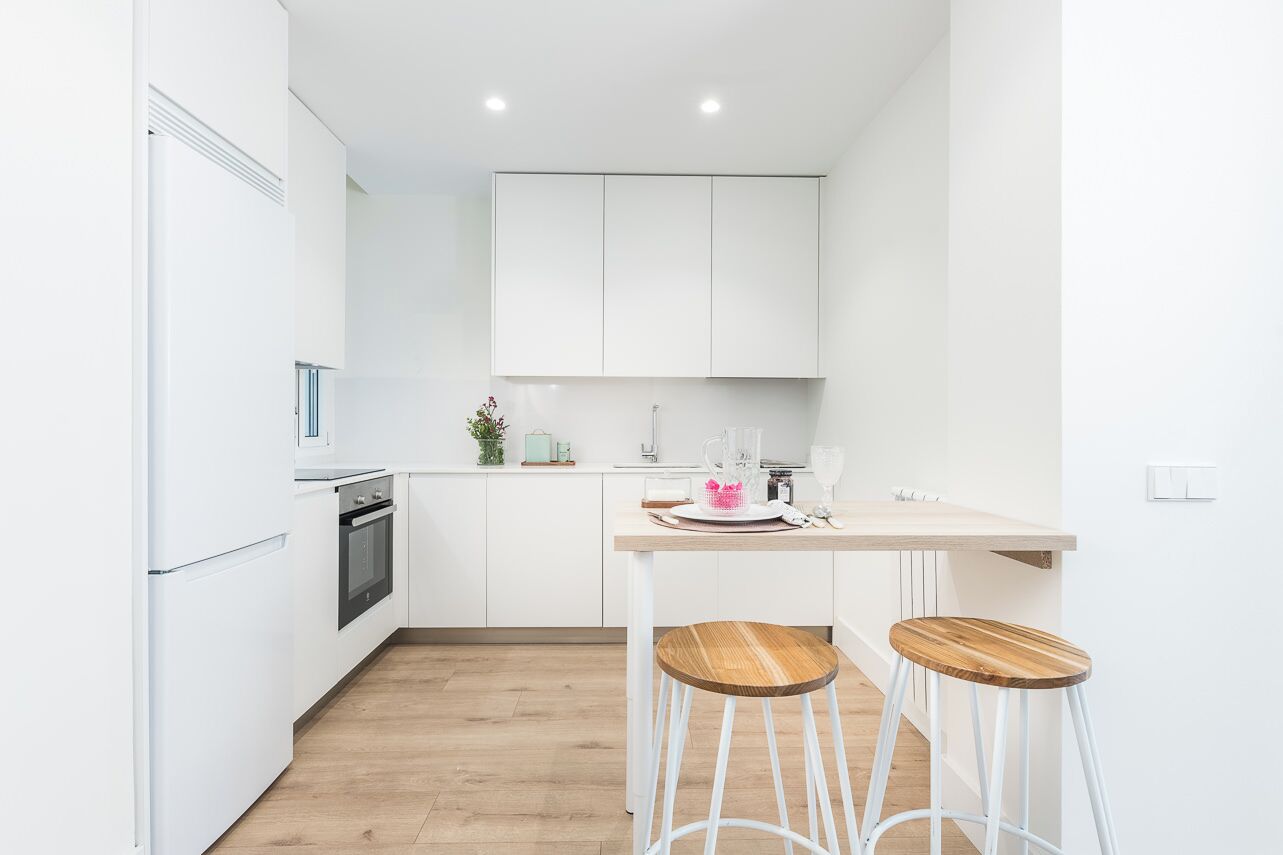 Een moderne keuken met witte kasten, een houten aanrecht en twee barkrukken.