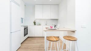 A modern kitchen with white cabinetry, a wooden countertop, and two stools. - Doctor Castelo LXIV - Two Bedroom Apartment, Sleeps 3 (Madrid)