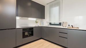 Een moderne keuken met grijze kastjes, een inbouwoven en een raam boven de gootsteen.