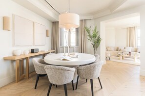 A modern dining area with a round table, four chairs, a hanging light fixture, and a large window with curtains. - Canalejas II - Two Bedroom Apartment, Sleeps 4 (Madrid)
