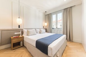 A hotel room with a large bed, bedside tables, a nightstand, and a window with curtains. - Canalejas II - Two Bedroom Apartment, Sleeps 4 (Madrid)