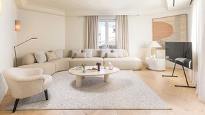 Ein modernes Wohnzimmer mit einem Ecksofa, einem runden Couchtisch, einer Stehlampe und einem Flachbildfernseher.