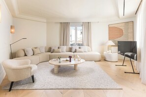 A modern living room with a sectional sofa, a round coffee table, a floor lamp, and a flat-screen TV. - Canalejas II - Two Bedroom Apartment, Sleeps 4 (Madrid)