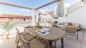 Eine Dachterrasse mit Holztisch, Korbstühlen, einer Couch und Topfpflanzen.
