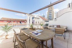 A rooftop terrace with a wooden table, wicker chairs, a sofa, and potted plants. - Canalejas II - Two Bedroom Apartment, Sleeps 4 (Madrid)