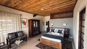 A bedroom with a wooden ceiling, a bed with a headboard, a sofa, a cabinet, and a window with curtains.
