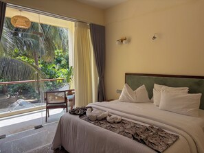 A hotel room with a bed, a chair, a window with curtains, and a view of greenery outside. - Mora Mila (Arugam Bay)