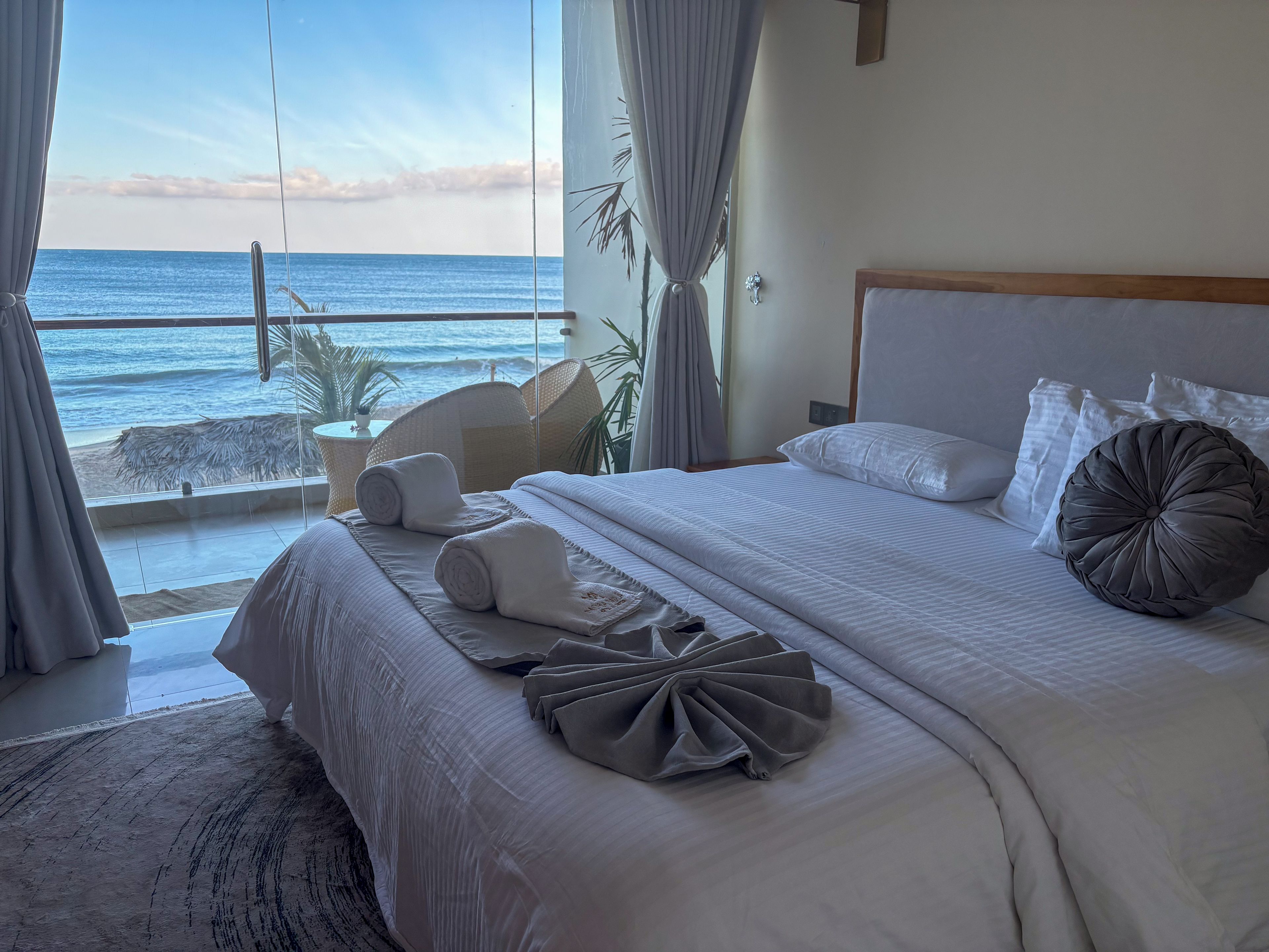 Ein Hotelzimmer mit einem großen Bett, Meerblick und einem Balkon mit Korbstuhl.