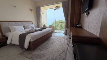 A hotel room with a large bed, a flat-screen TV mounted on the wall, and a balcony with a view of the sea.