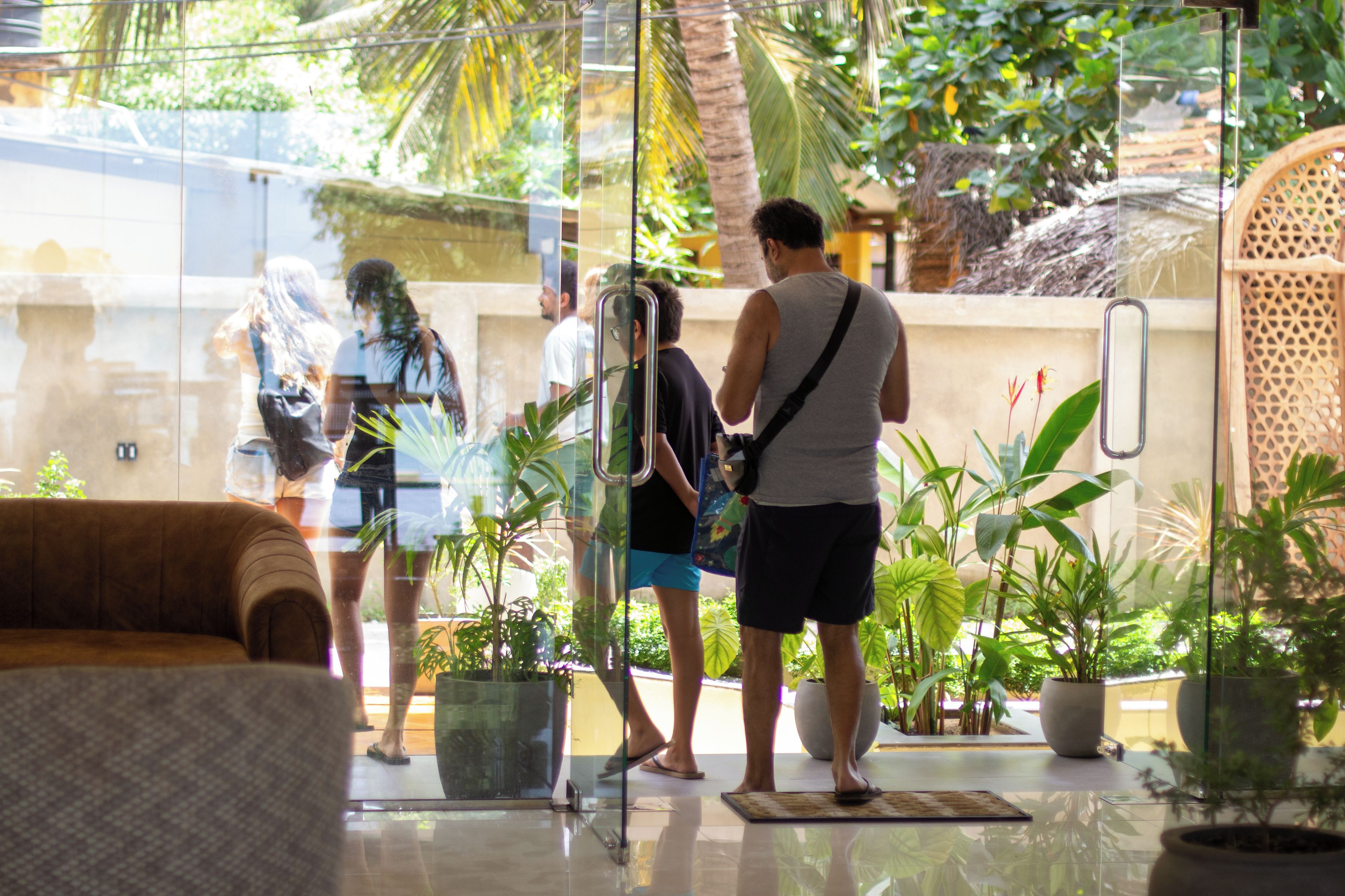 A glass-walled lobby with indoor plants, a seating area, and a visible outdoor view.