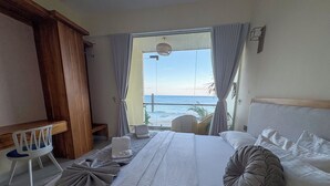 A hotel room with a bed, a chair, a small table, and a view of the ocean. - Mora Mila (Arugam Bay)