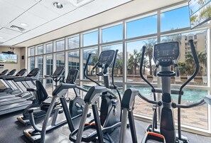 A gym with treadmills and exercise bikes, large windows, and a pool view. - Beach View Top Floor Condo | Skywalk Beach Access | Pools | Sleeps 6 | BEACHBALL PROPERTIES (Gulf Shores)