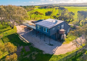 A modern house with a solar panel roof, a water tank, and a fenced yard.