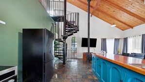 Una cucina con un frigorifero nero, un armadietto blu, un soffitto in legno e una scala a chiocciola.