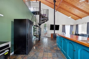 A kitchen with a black refrigerator, a blue cabinet, a wooden ceiling, and a spiral staircase.