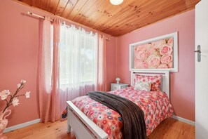 Un dormitorio con techo de madera, cama con ropa de cama floral, mesita de noche y pared rosa.
