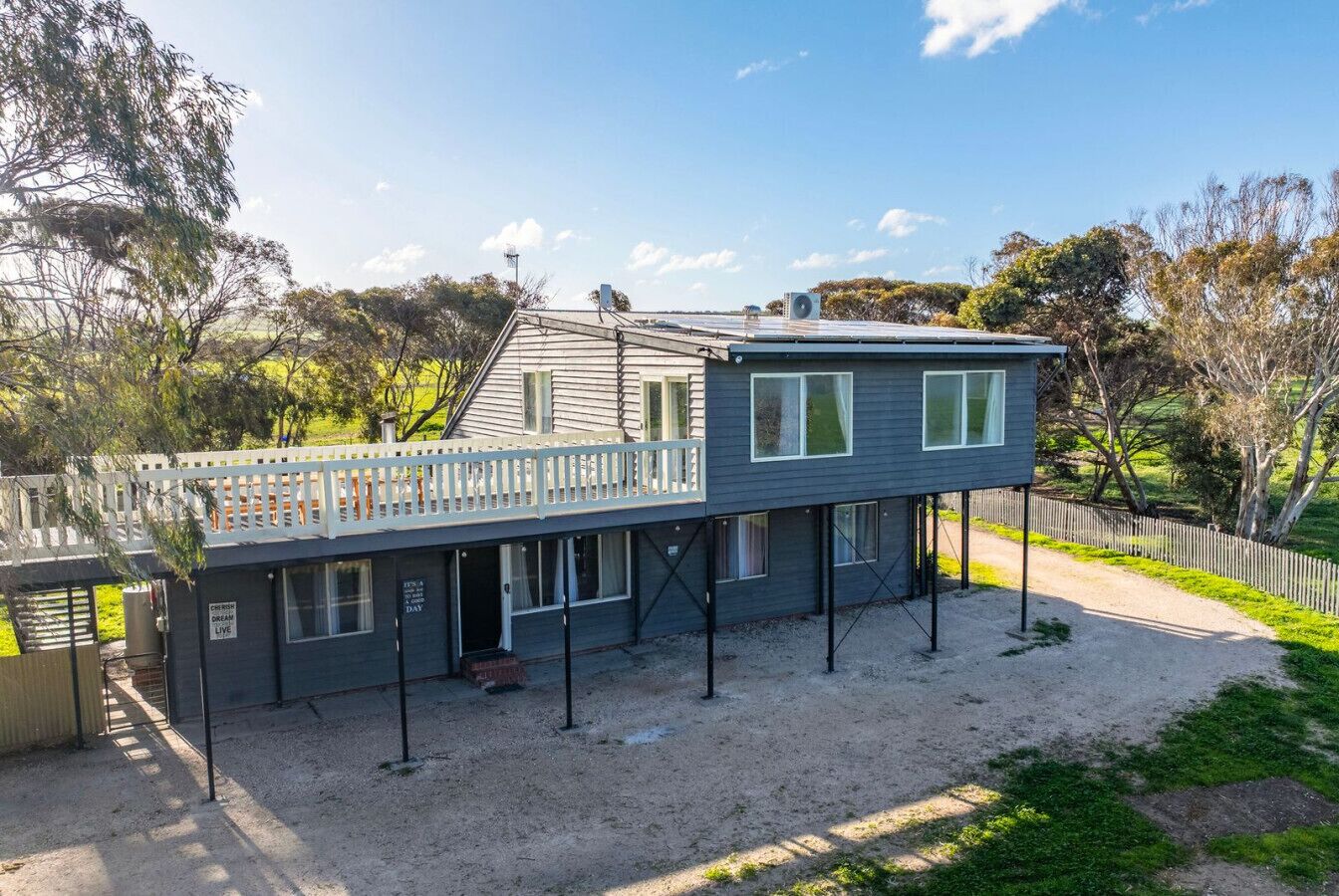 Ein zweigeschossiges Haus mit Balkon, überdachter Veranda und Kiesweg.