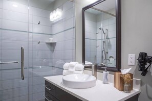Een moderne badkamer met een douchecabine van glas, een grote spiegel, een witte wastafel en een handdoekhouder.