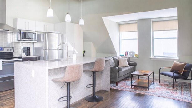 A modern kitchen with a central island, bar stools, a gray sofa, and a coffee table. - Downtown Luxury 1BR Loft · Walkable · Sleeps 4 (Milwaukee)