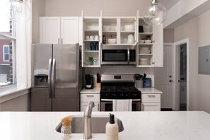 A modern kitchen with white cabinetry, a stainless steel refrigerator, a microwave, and a gas stove.