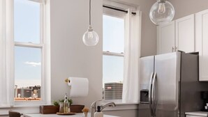 Cocina moderna con una isla central, taburetes de bar, electrodomésticos de acero inoxidable e iluminación colgante.