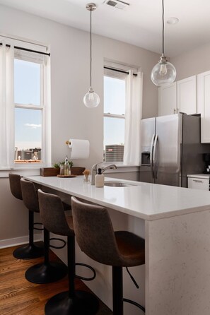 A modern kitchen with a central island, bar stools, stainless steel appliances, and pendant lighting. - Penthouse and Private Rooftop with Skyline Views, Grill, and Fire Pit - Sleeps 6 (Chicago)