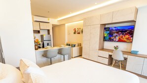 Ein modernes Hotelzimmer mit Bett, Schreibtisch, Fernseher und einer Küchenzeile.