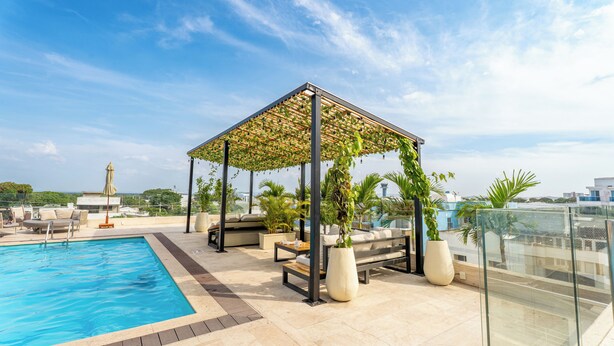 Ein Poolbereich auf dem Dach mit Glasgeländer, Liegebereichen und einer Pergola mit Kletterpflanzen.