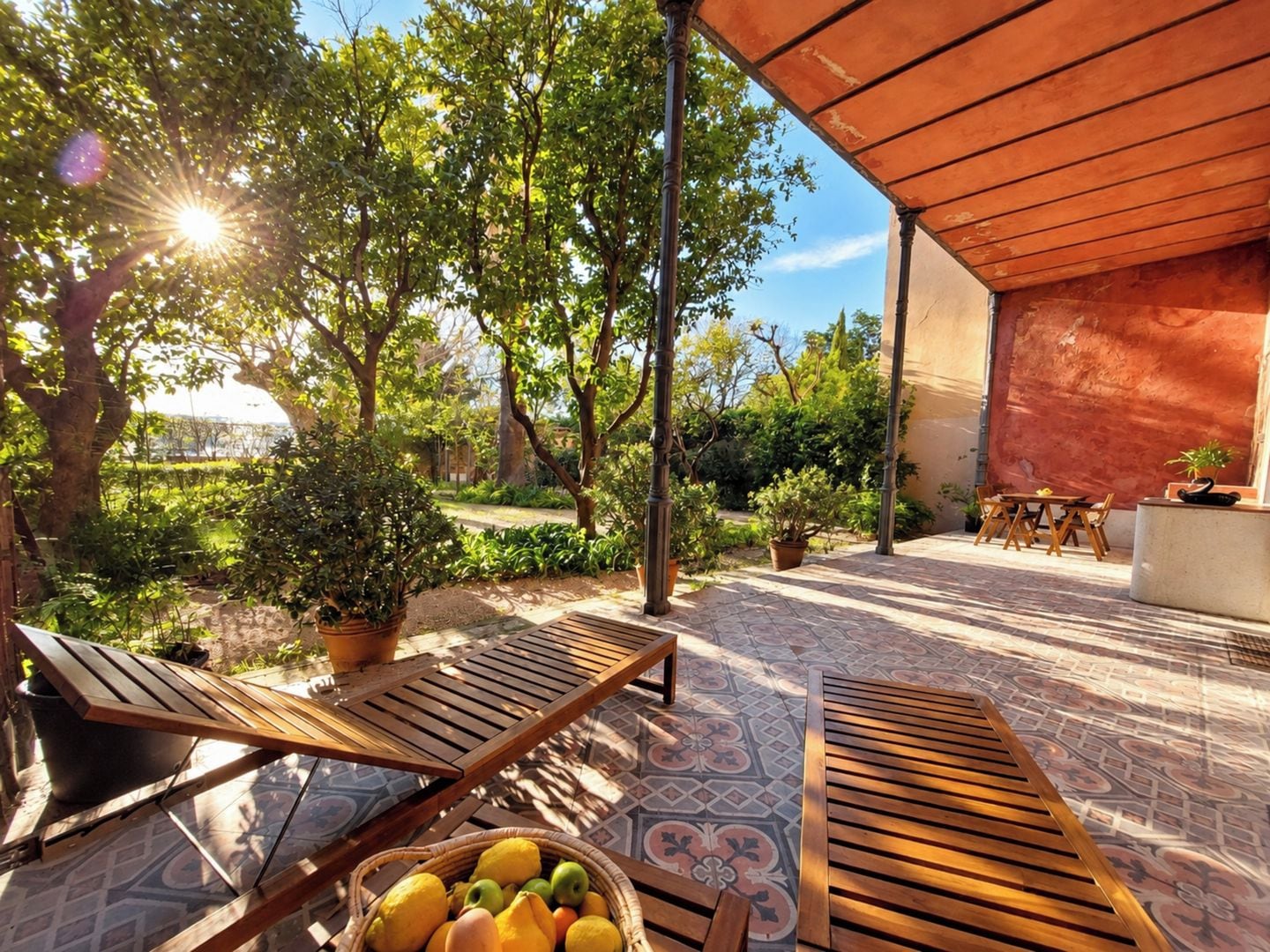 An outdoor patio with wooden furniture, a tiled floor, and potted plants.