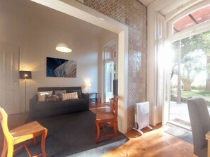 A living room with a sofa, a dining table, and chairs, a radiator, and a view of the outdoors. - Lisbon Hideaway with private sunny Garden (Lisbon)