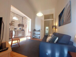 A living room with a blue sofa, a TV, and a kitchen in the background. - Lisbon Hideaway with private sunny Garden (Lisbon)