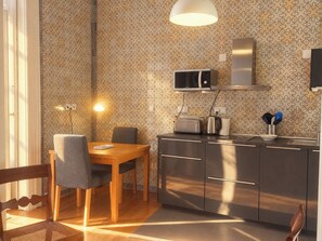 A modern kitchen with a dining area, featuring a microwave, toaster, and kettle on the counter, and a wooden table with chairs. - Lisbon Hideaway with private sunny Garden (Lisbon)