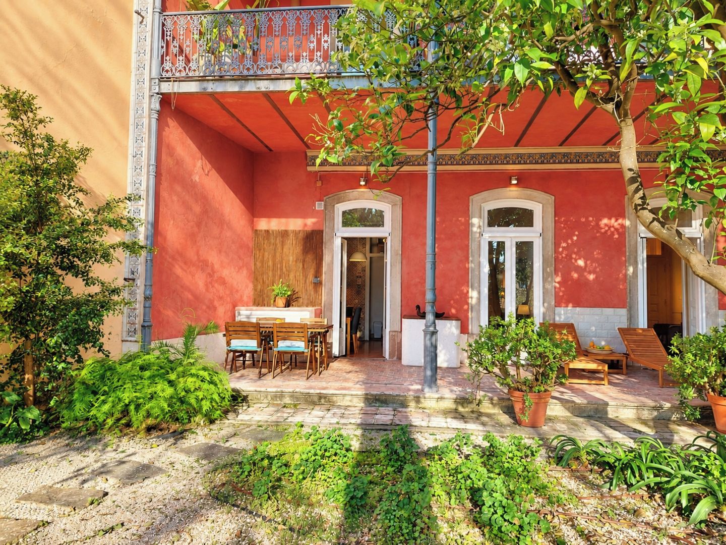 A courtyard with a red building, a dining area with chairs and a table, and potted plants.