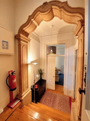 A hallway with a wooden door frame, a fire extinguisher, a floor lamp, and a patterned rug. - Lisbon Hideaway with private sunny Garden (Lisbon)
