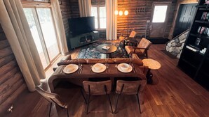A log cabin interior with a dining area, wooden walls, a fireplace, and a television. - Edgewater Lodge: Riverfront Family Fun in Grayling (Grayling)