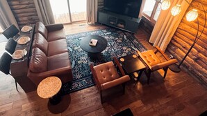 A modern living room with a leather sofa, a coffee table, a TV, and a patterned rug. - Edgewater Lodge: Riverfront Family Fun in Grayling (Grayling)