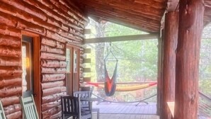 A log cabin with a porch, outdoor seating, and a hammock. - Edgewater Lodge: Riverfront Family Fun in Grayling (Grayling)