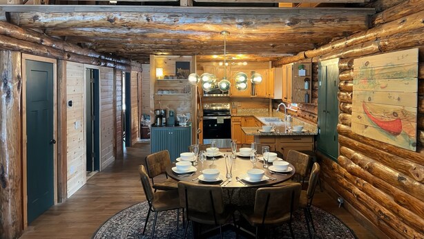 A log cabin interior with a dining area, kitchen, and a loft bedroom. - Edgewater Lodge: Riverfront Family Fun in Grayling (Grayling)